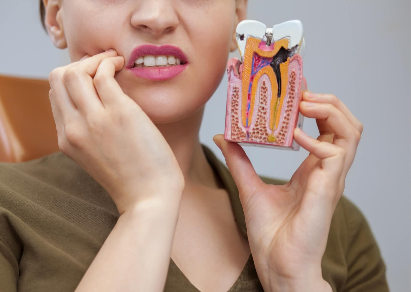 Person experiencing tooth discomfort while holding a dental model showing tooth decay, illustrating why a cavity cannot heal itself once a hole has formed in the tooth.