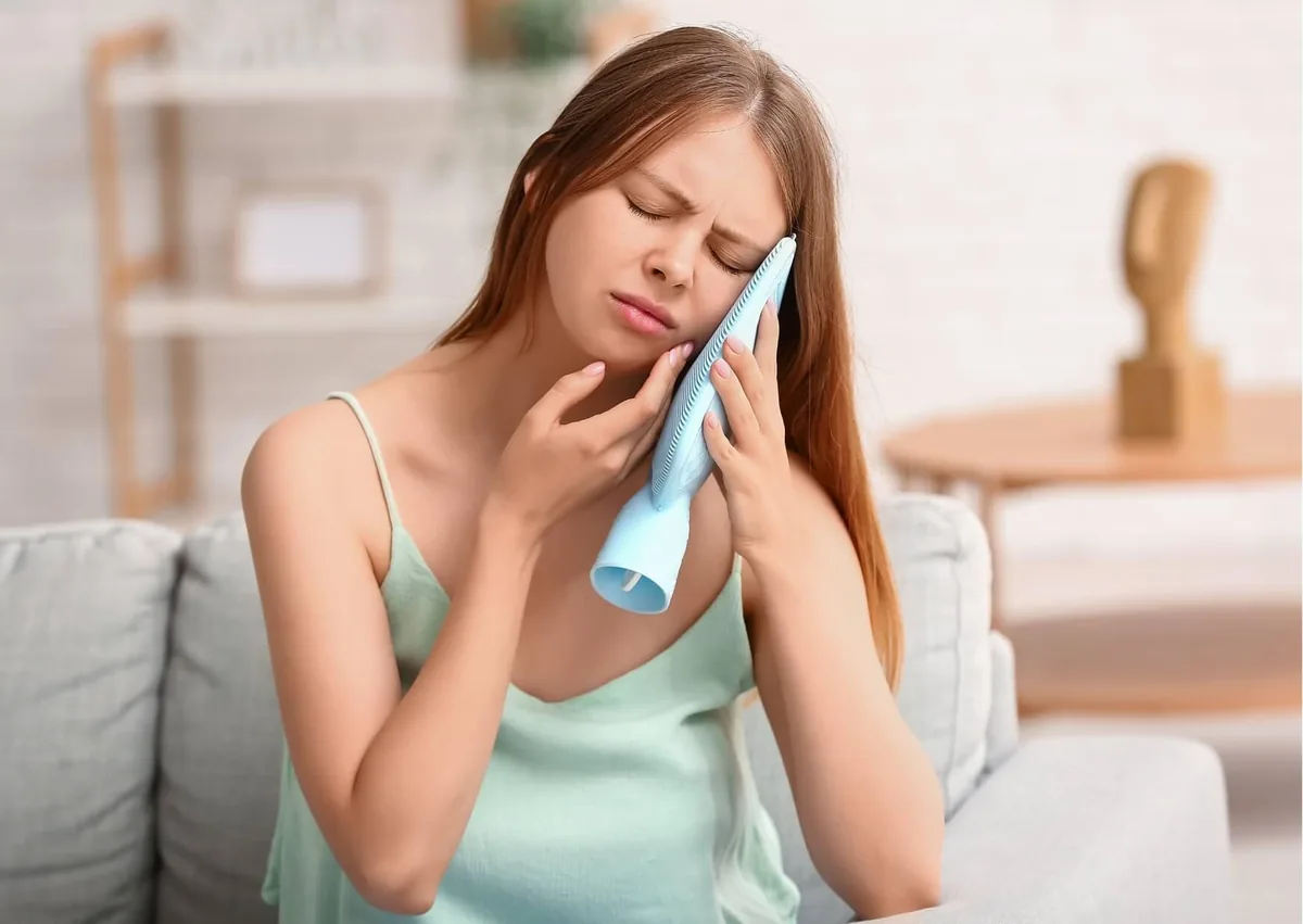 Woman applying a cold compress to her cheek for wisdom tooth pain relief.