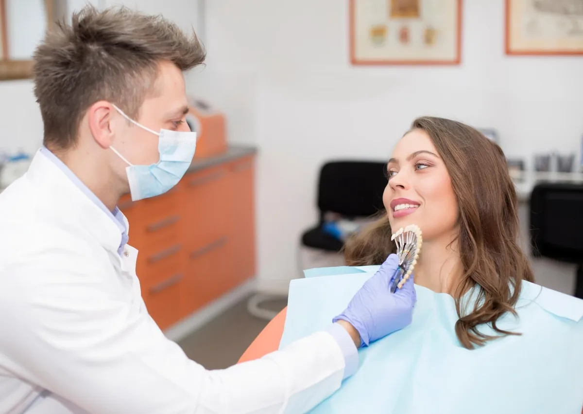 Dentist showing a patient tooth shades while discussing dental crown types and costs.